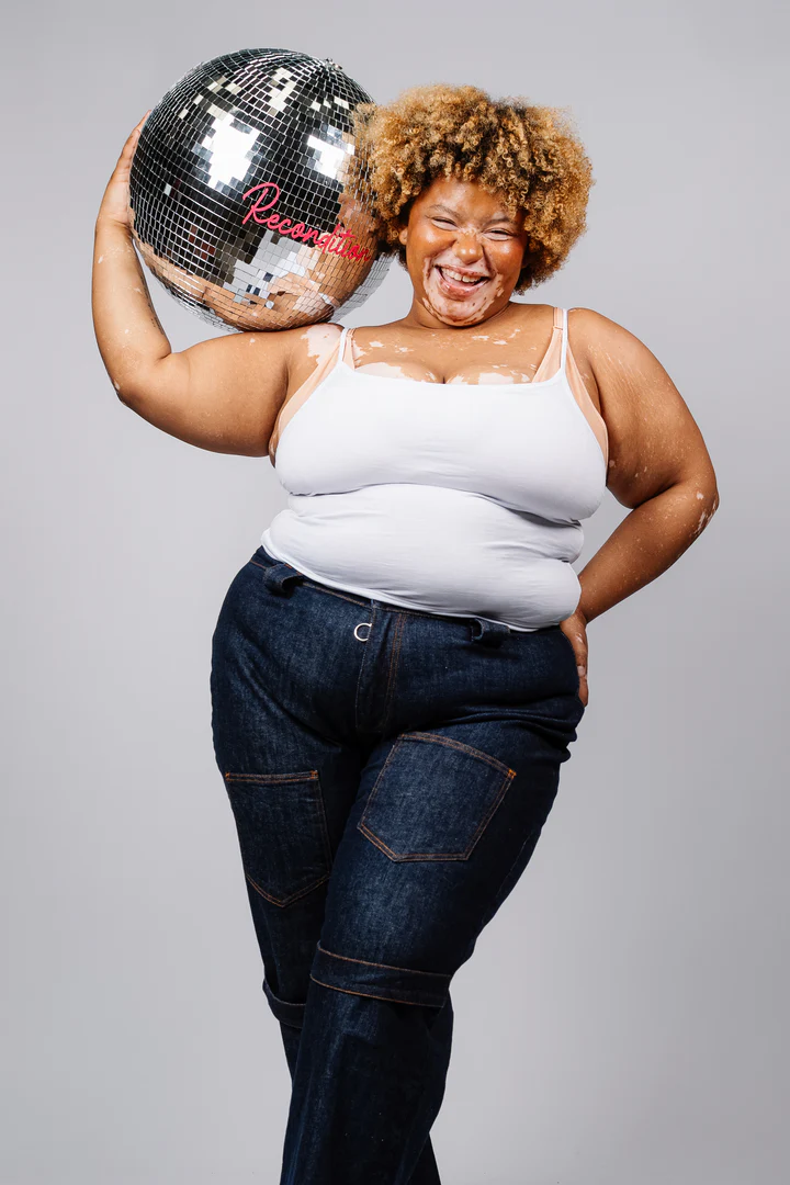 Curvy model wears Recondition jeans and balances a mirrorball on her shoulder